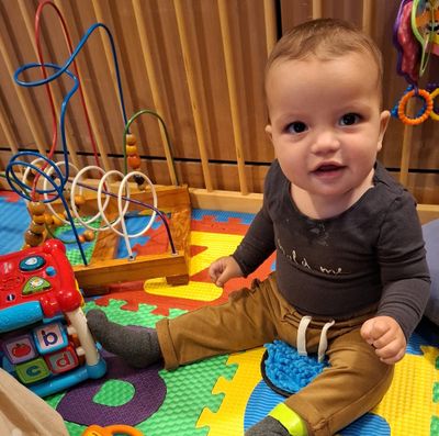 A baby sitting on a colourful play mat surrounded by toys